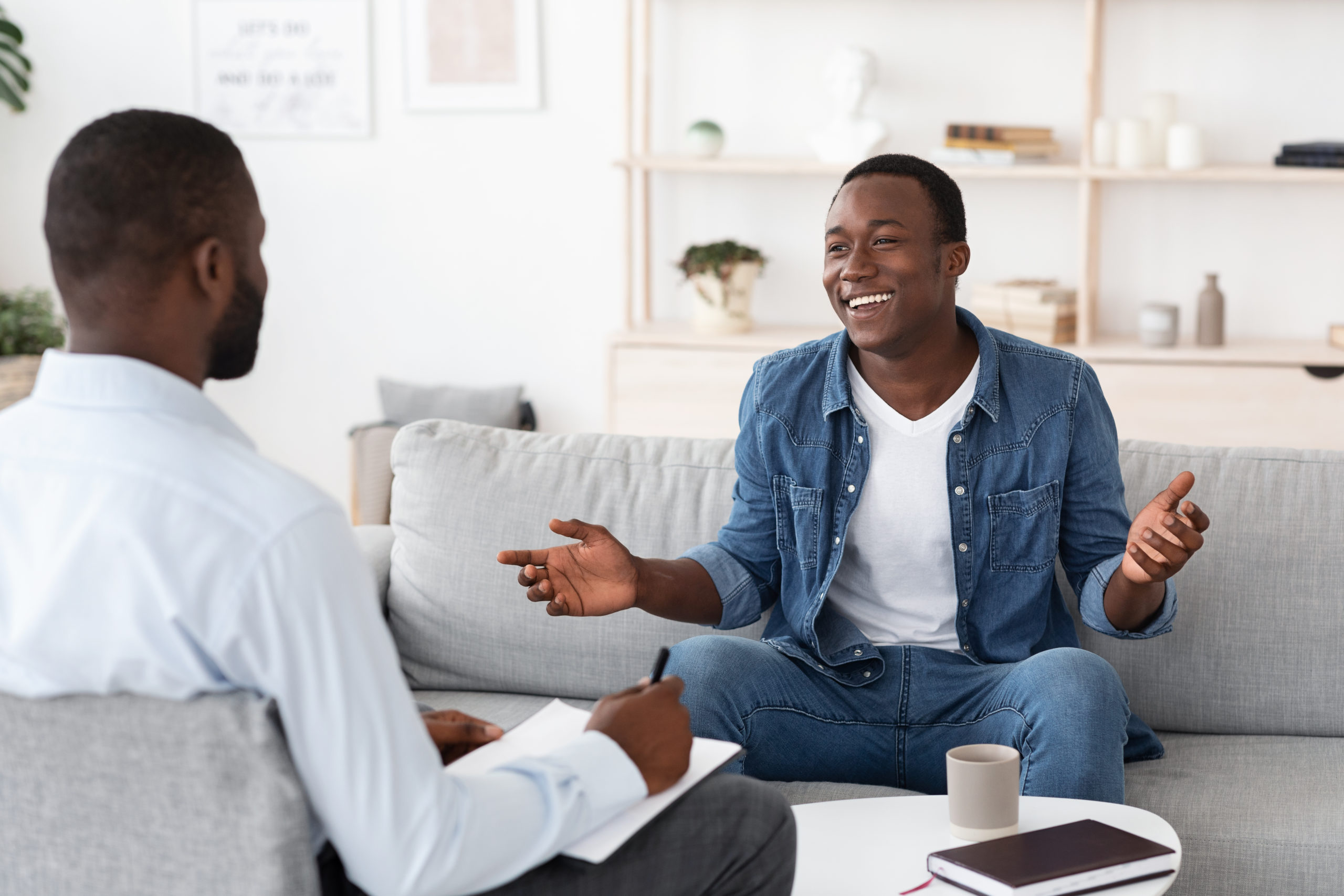 Cheerful black man talking to psychologist and sharing his progress.